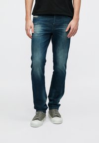 Tumesinised teksapüksid tavapärase lõikega, pleekinud detailidega ja klassikalise viie taskuga, kantud koos hallide tossudega.