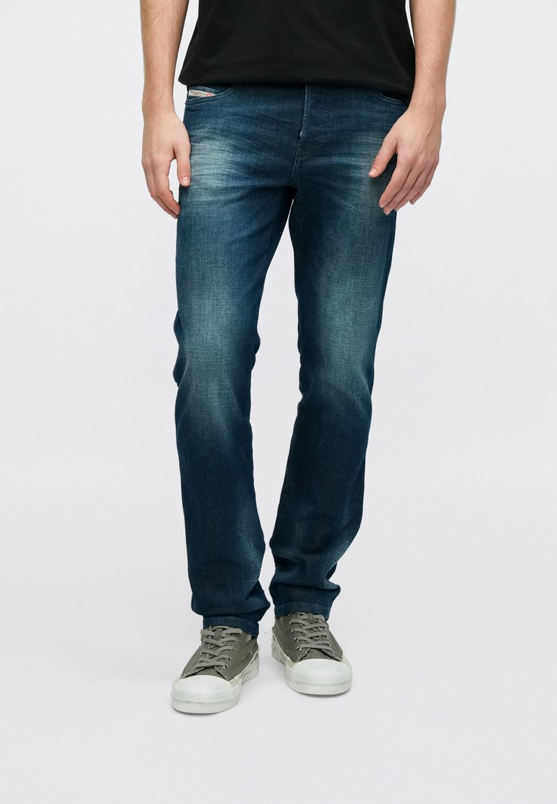 Tumesinised teksapüksid tavapärase lõikega, pleekinud detailidega ja klassikalise viie taskuga, kantud koos hallide tossudega.