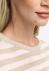 Bež ja valge triibuline sviiter ribitud kaeluse jaotusega. Suurendatud vaade toob esile pehme tekstuuri ja õmblused kaeluses.