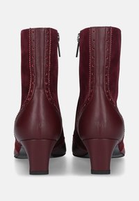 Bordeaux enkelboots van suede en leer, met een gebogen hak, zigzagstiksel en decoratieve gaatjes langs de naden.
