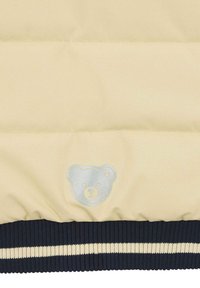 Giacca imbottita beige con una superficie liscia, caratterizzata da un logo di un orso blu chiaro e un orlo a coste blu scuro con strisce color crema.