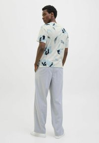 Camiseta de manga corta de color claro con diseño floral azul y negro, combinada con pantalones sueltos de color gris claro y zapatillas blancas.