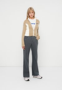 Beige og hvit cropped zip-up genser over en grafisk T-skjorte, kombinert med grå vide jeans og lyse joggesko. Minimalistisk design, glatt tekstur.