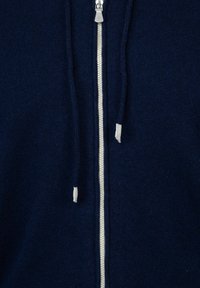 Felpa con zip di colore blu navy, con una texture morbida, zip leggera e cordini. Presenta un design classico e dettagli a costine lungo i bordi.