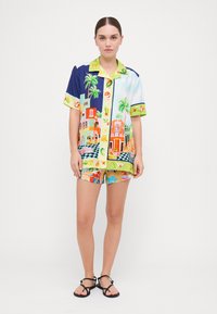 Camicia a maniche corte colorata con una vivace stampa di paesaggio urbano. Abbinata a pantaloni corti con fantasia in tonalità brillanti. Tessuto leggero e casual.