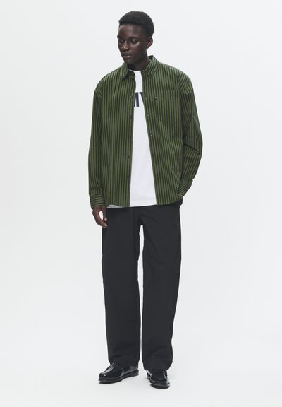 Green and black striped button-up shirt, long sleeves, worn over a white t-shirt, paired with black trousers and shoes. Simple design, casual fit.