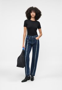 Høyt midjede blå denimjeans med sidestriper, kombinert med en tettsittende svart t-skjorte og svarte ankelstøvler. Bærer en svart veske.