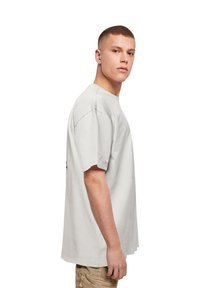 Lys grå bomulls t-skjorte med korte ermer og avslappet passform, med minimalistisk design, sømdetaljer og logo på ryggen.