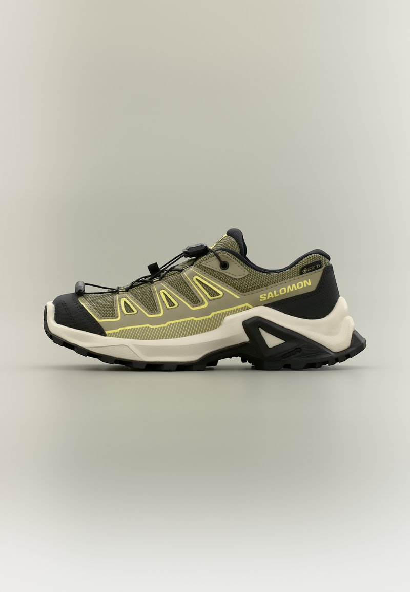 Πράσινο ελιάς και μαύρο παπούτσι για trail running με μπεζ σόλα, σύστημα γρήγορου δέσιμου κορδονιών και μάρκα Salomon στο πλάι.