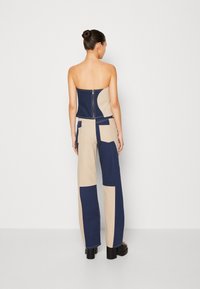 Jumpsuit patchwork blu e beige con bustino aderente senza spalline e pantaloni a gamba larga, dotato di zip posteriore e tasche.
