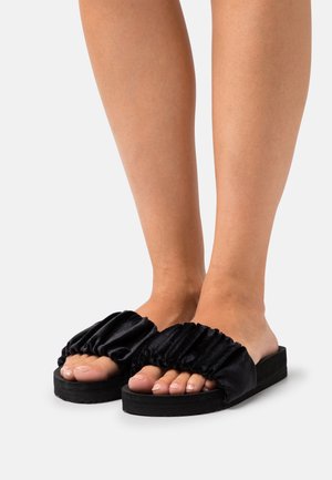 Black slide sandals with a gathered satin strap and a thick rubber sole, exposing toes and featuring a cushioned footbed.