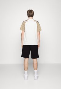 Kortärmad skjorta i vitt med bruna ärmar, med ett strukturerat mönster på axlarna. Matchas med svarta shorts och vita sneakers.