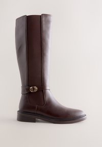 Cizmă înaltă din piele maro închis, cu panou elastic lateral și cataramă decorativă aurie, talpă plată și vârf rotunjit.