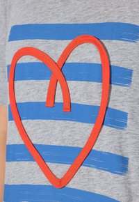 Camiseta gris con rayas horizontales en azul y blanco, con un diseño prominente de un corazón rojo hecho de tela trenzada en el centro.