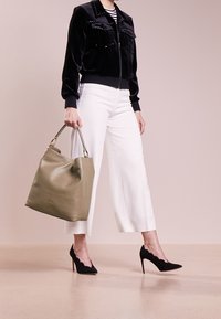 Chaqueta de terciopelo negro con cierre de cremallera y bolsillos de parche, pantalones blancos de pierna ancha y un suave bolso tote de cuero verde oliva. Tacones puntiagudos negros.