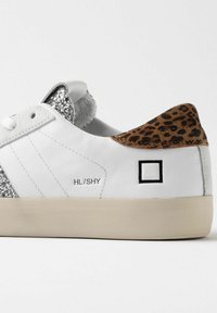 Hvide sneakers med glitrende sølv sidepanel, brun leopardmønstret hæl og sort firkantet logo. Har en flad, beige gummisål.