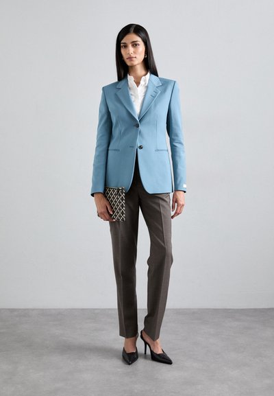 Light blue tailored blazer with a single button closure, paired with gray slim-fit trousers and black pointed heels. Holding a patterned clutch.