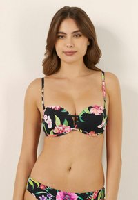 Svart bikiniöverkär med blommönster som har rosa och gröna blommor, med undertråd för stöd och tunna justerbara axelband. Utmärkande sidokut.