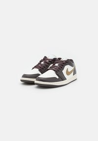 Nike tenisky s bílým koženým svrškem a tmavě hnědými akcenty, zlatým logem swoosh, hnědými tkaničkami a gumovou podrážkou.