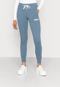 Light blue sweatpants made of cotton blend, with a drawstring waist and tapered legs, featuring a small white logo on the thigh.