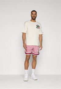 Short cream t-shirt with NY logo and floral design, paired with pink mesh shorts featuring white stripes and floral embroidery, worn with white sneakers.