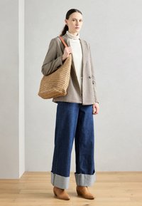 Woven beżowa torba, kraciasty brązowy blezer na kremowym golfie, niebieskie jeansy z szerokimi nogawkami i mankietami z denimu oraz brązowe buty na obcasie.