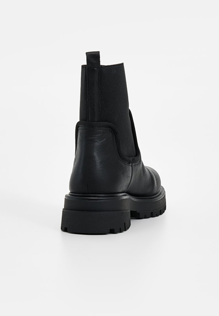 Stivale alla caviglia in pelle nera con pannelli laterali elastici, suola spessa e linguetta sul retro. Presenta una superficie texturizzata e un design robusto.