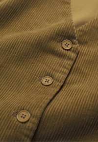 Smeđi kordurol s vertikalnim rebrima, s četiri okrugla, smeđa dugmeta duž prednjeg preklopa. Mekana tekstura, minimalan sjaj.