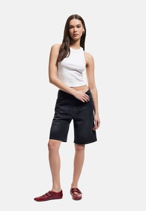 Top corto blanco con ribetes, combinado con pantalones cortos bermuda de mezclilla azul oscuro. El modelo lleva zapatos rojos. Diseño sencillo, ajustado y de aspecto casual.