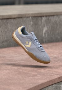 Γκρι και μπεζ αθλητικό παπούτσι με σόλα από καουτσούκ να αιωρείται πάνω από ροζ σκάλες από σκυρόδεμα σε υπαίθριο χώρο.