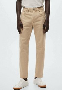 Pantalones de algodón beige con un corte recto, que cuentan con bolsillos frontales y cremallera, combinados con zapatillas blancas.