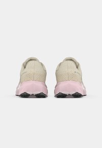 Et par beige og rosa treningssko vist fra baksiden, med teksturert hældesign og svarte mønstrede såler.