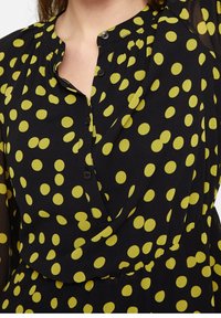 Schwarzes Kleid mit großen gelben Punkten, mit einem geknöpften Ausschnitt, gerafftem Stoff und einer lässigen Form. Weicher Stoff mit fließendem Design.