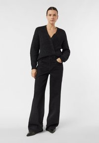 Czarny, prążkowany sweter o kroju kopertowym z głębokim dekoltem w serek i długimi rękawami, zestawiony z czarnymi, rozszerzanymi dżinsami z subtelnymi metalicznymi drobinkami i kieszeniami.