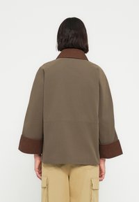 Καφέ βαμβακερό σακά κι με φαρδύ γιακά, με αντιθετικές μανσέτες από σκουρόχρωμο καφέ κορδωτό ύφασμα και χαλαρή εφαρμογή. Απλή πλάτη, χωρίς εμφανείς κλεισίματα.