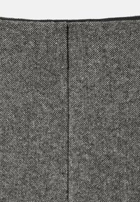 Un tejido gris texturizado presenta un patrón tejido y una costura vertical, con un ribete oscuro a lo largo del borde superior.