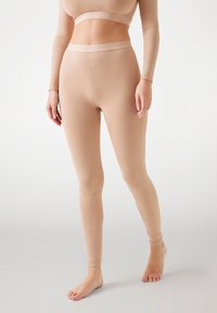 Nude leggings tillverkade av ett stretchigt material, med en sömlös design, en åtsittande silhuett och ett elastiskt midjeband.