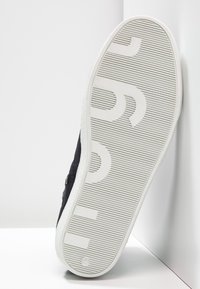 Baskets noires avec un dessus texturé, semelle en caoutchouc blanche. Présente des lettres audacieuses sur la semelle et une finition lisse le long des bords.