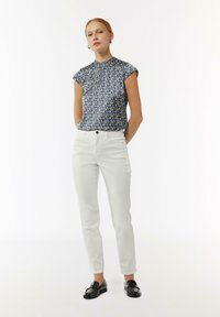Bluse mit Blumenmuster in marineblau und kurzen Ärmeln, kombiniert mit weißen Slim-Fit-Hosen und schwarzen Slippern, mit einer glatten Textur.