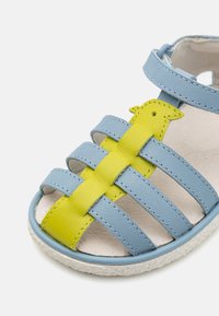 Blaues Leder-Sandale mit gelben Akzenten, mehreren Riemen und einer strukturierten weißen Sohle. Verfügt über ein vogelförmiges Detail am Riemen.