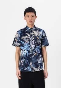 Chemise à manches courtes avec un fond bleu marine orn�ée de motifs de feuilles tropicales et d'oiseaux en bleu clair, blanc et orange. Tissu en coton.