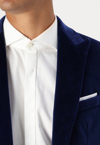 Navy velours blazer met notch-lapels, vergezeld van een wit shirt met een verborgen knoopsluiting en een pochet in de borstzak.