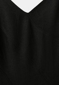 Detailný záber na čiernu tkaninu s výstrihom do tvaru písmena V a viditeľnými diagonálnymi švami na hladkom povrchu.