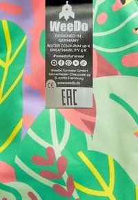 Tissu coloré présentant des feuilles vertes et des formes roses. Accompagné d'une étiquette d'entretien avec une marque, des symboles et des informations sur la résistance à l'eau.