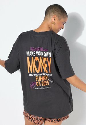 Camiseta oversized negra con texto colorido en la parte posterior: "HAZ TU PROPIO DINERO Y CASA CON ALGUIEN GRACIOSO 07/2025", acompañada de pantalones cortos de estampado de leopardo.