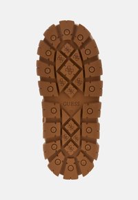 Rudas gumos bato padas su tekstūru, turintis šešiakampių ir apvalių formų, pažymėtas ženklu "GUESS" ir dydžiu "39."