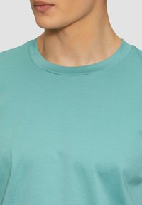 T-shirt in cotone turchese con design a girocollo. Presenta una texture liscia, maniche corte e dettagli delle cuciture minimi.