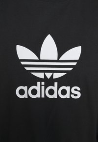 Sort bomulds T-shirt med et stort hvidt trefoil-logo og "adidas" tekst under, begge tydeligt vist på forsiden.
