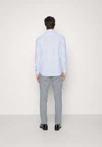 Camisa de manga larga en azul claro con un patrón sutil, combinada con pantalones gris claro y zapatos negros, vista desde atrás.