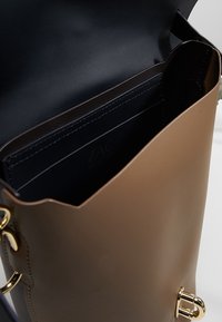 Hnědá kožená kabelka s hladkým povrchem, vybavená zlatými akcenty a černým interiérem se sloty na karty. Kabelka bez víka.